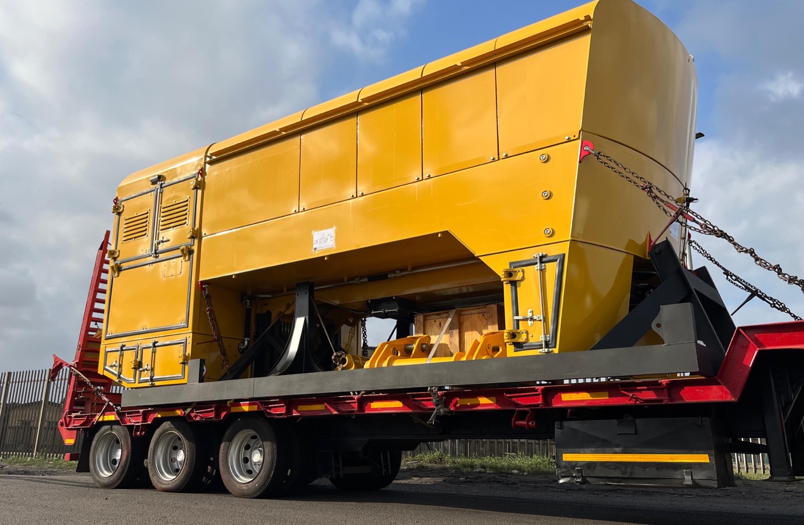 Oversized yellow heavy machinery secured on a lowboy trailer for transport