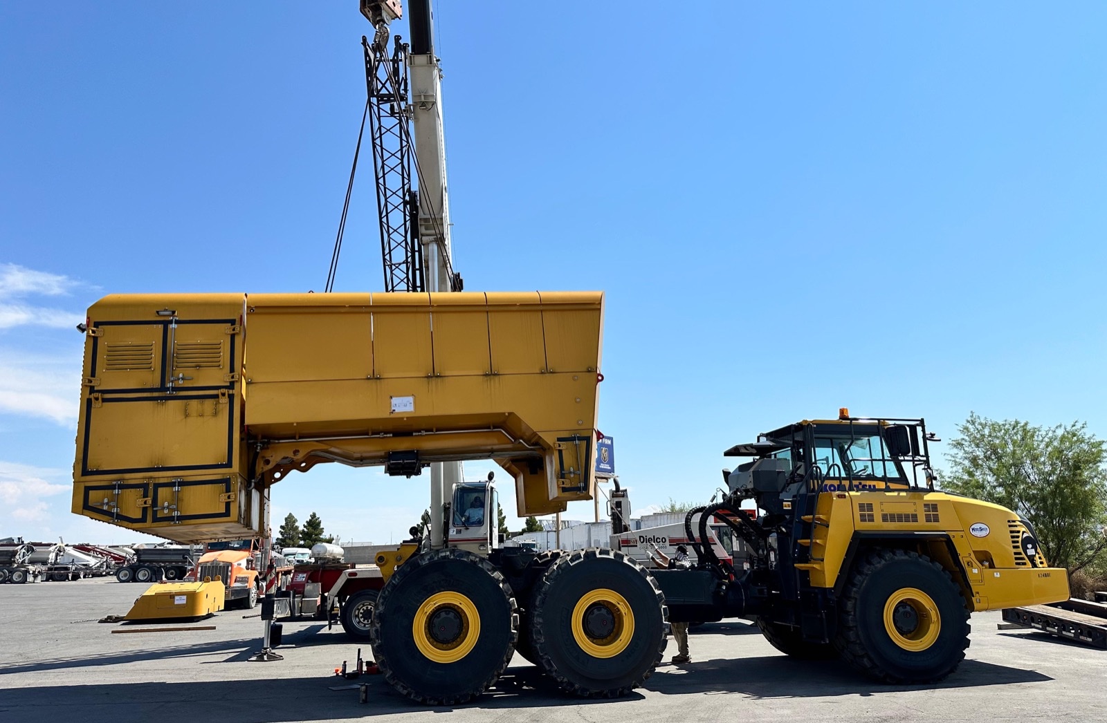Crane lifting an oversized articulated dump truck body with a wheel loader