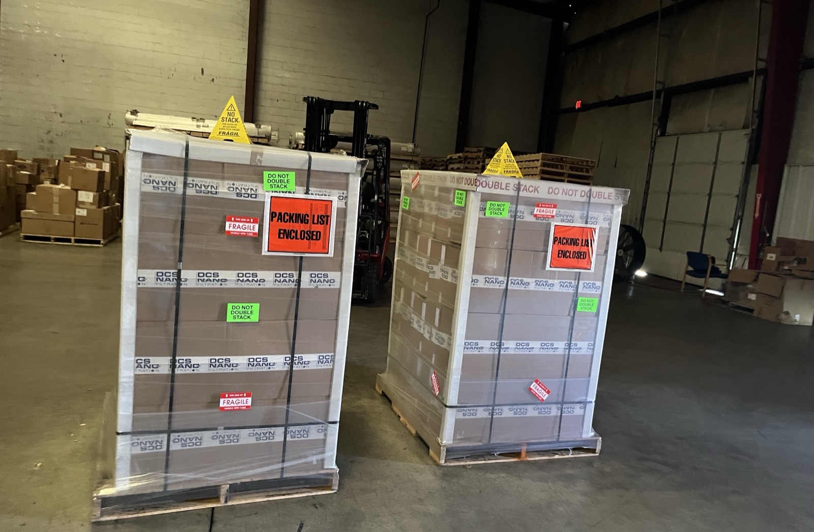 Shrink-wrapped freight pallets staged in a warehouse with a forklift